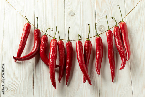 Red hot chili peppers are dried on a thread. On a white wooden background.