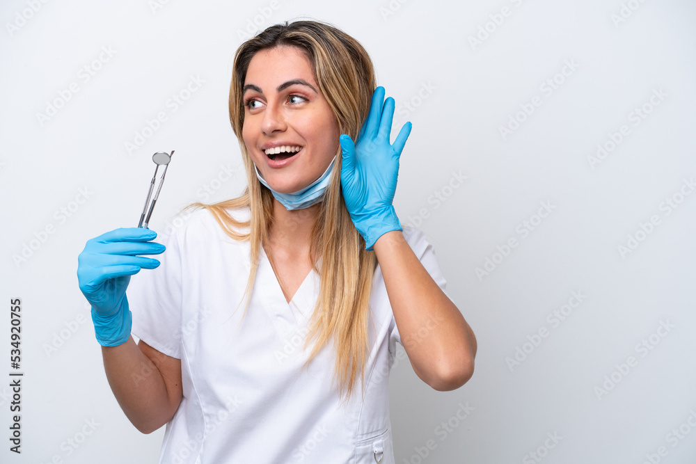 Dentist woman holding tools isolated on white background listening to something by putting hand on the ear Dentist woman holding tools isolated on white background listening to something by putting hand on the ear