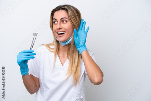 Dentist woman holding tools isolated on white background listening to something by putting hand on the ear