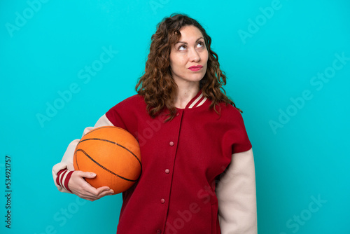 Young caucasian basketball player woman isolated on blue background and looking up