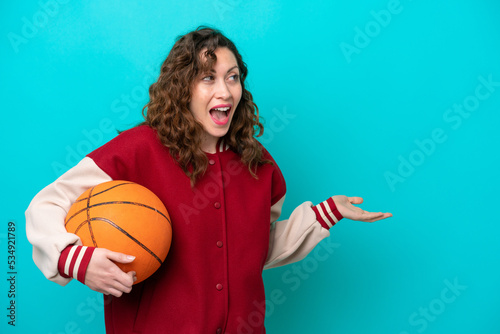 Young caucasian basketball player woman isolated on blue background with surprise expression while looking side © luismolinero