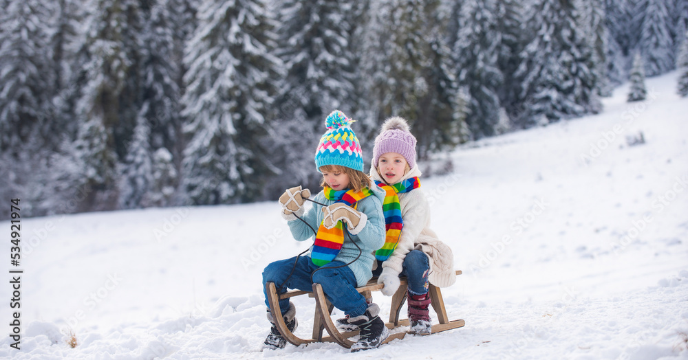 Happy little boy and girl sledding in winter. Kids sibling riding on snow slides in winter. Son and daughter enjoy a sleigh ride. Winter landscape with snow.