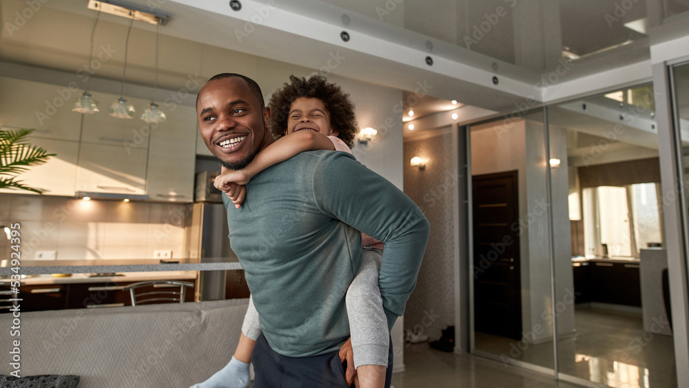 Joyful father carry little son piggyback at home