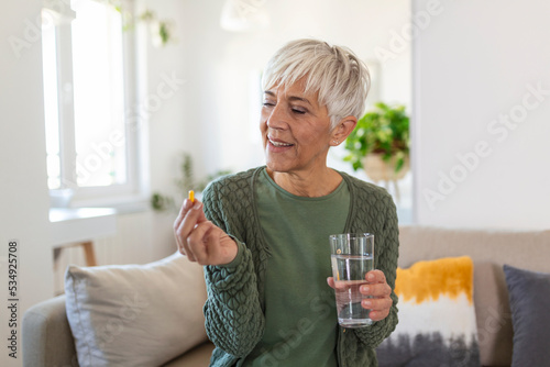 Quadro em tela Senior woman takes pill with glass of water in hand.