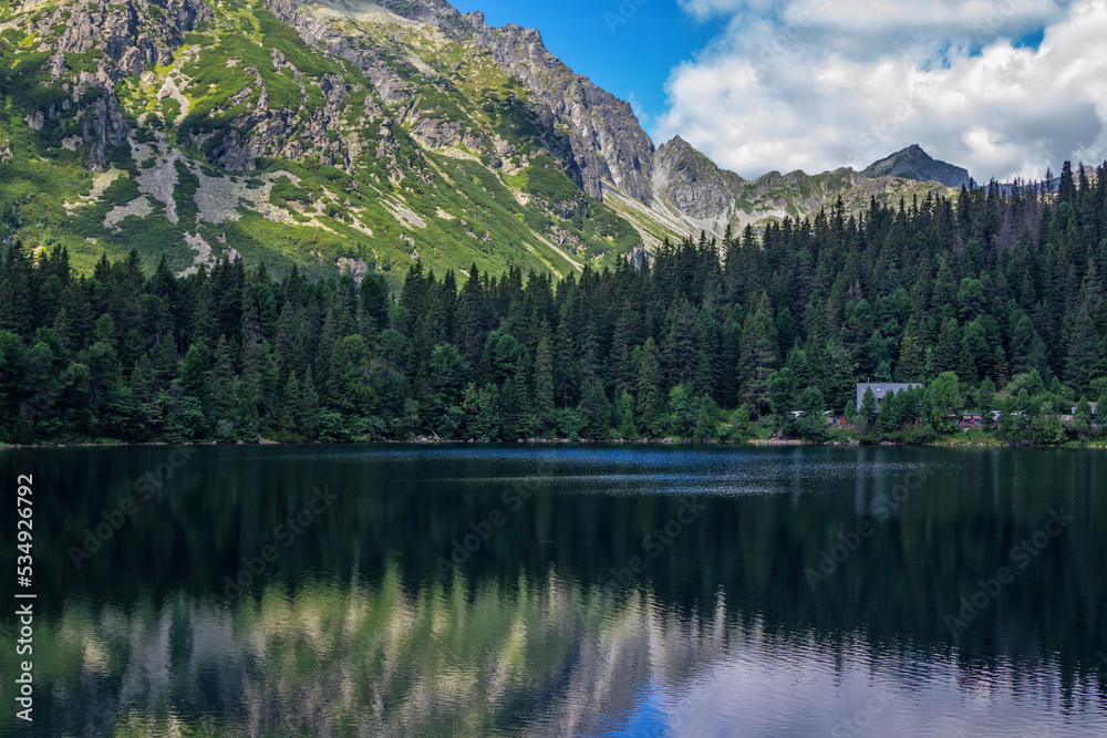 Beautiful summer landscape of High Tatras, Slovakia - Poprad lake, lush forest, reflecting on water surface, mountains and white clouds on the sky