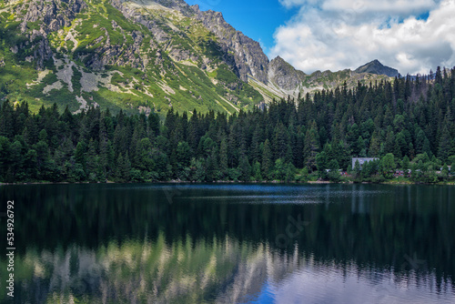 Beautiful summer landscape of High Tatras, Slovakia - Poprad lake, lush forest, reflecting on water surface, mountains and white clouds on the sky © elenakirey