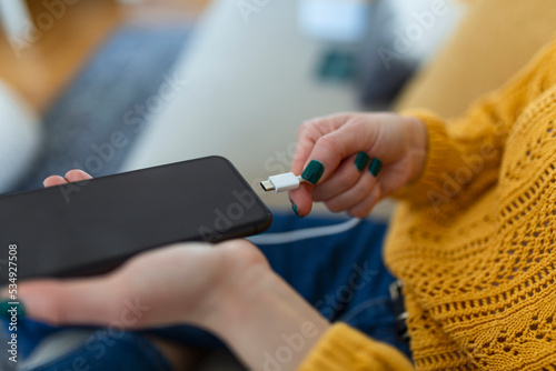 Woman hands plugging a charger in a smart phone. Woman using smartphone with powerbank, charging power to smart phone. Woman charging battery on mobile phone at home