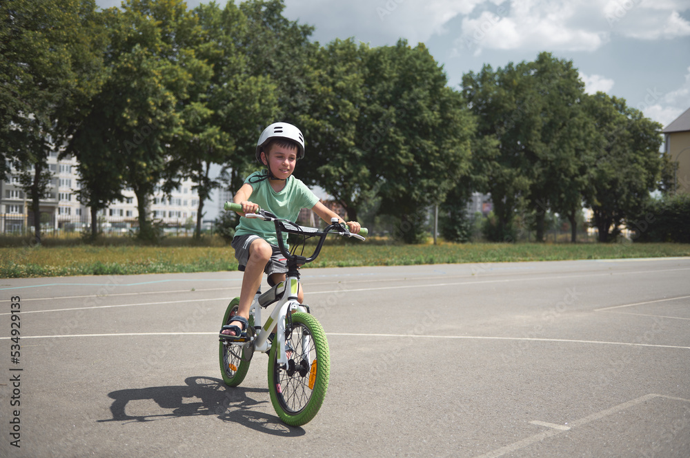 Elementary age Caucasian boy, sporty active child in sports helmet, learns extreme tricks and extreme cycling in city, cycling on the asphalt road outdoors. Sport. Active, healthy lifestyle concept