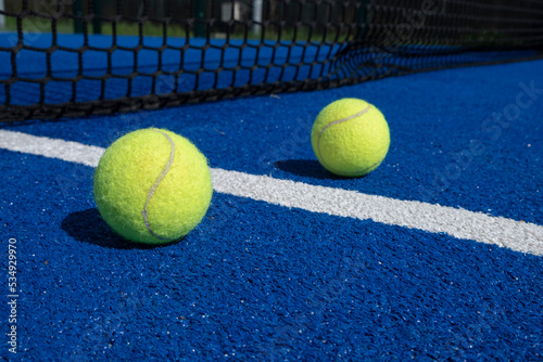 two balls near the net of a paddle tennis court