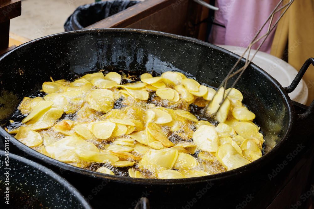 Frying sliced potatoes in oil and stirring with a slotted spoon Frying sliced potatoes in oil and stirring with a slotted spoon