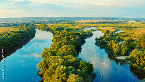 Aerial view above a beautiful landscape with a  river while sunset. Aerial view from drone flies over a beautiful summer landscape.