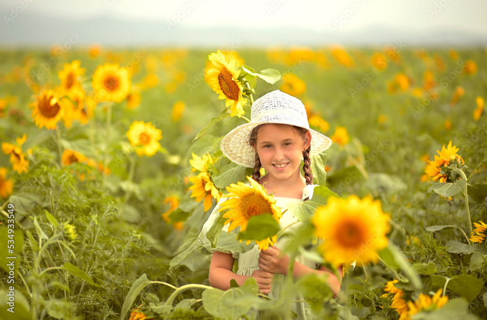 happy child girl in a green dress and white hat stands in a plait with yellow sunflowers smiling happy child girl in a green dress and white hat stands in a plait with yellow sunflowers smiling