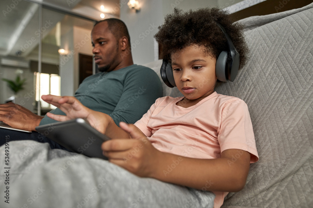 Fototapeta premium Boy use digital tablet while father type on laptop