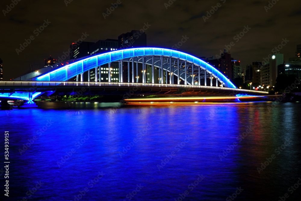 Naklejka premium ブルーにライトアップされた永代橋をくぐる屋形船の眩い軌跡