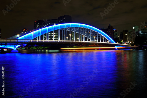 ブルーにライトアップされた永代橋をくぐる屋形船の眩い軌跡