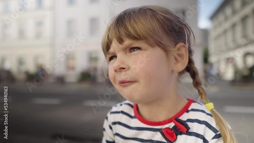 Little girl eating tasteless jelly candy on the street. Child first tastes harmful sweets. Unhealthy food. Portrait of a kid who eats. 