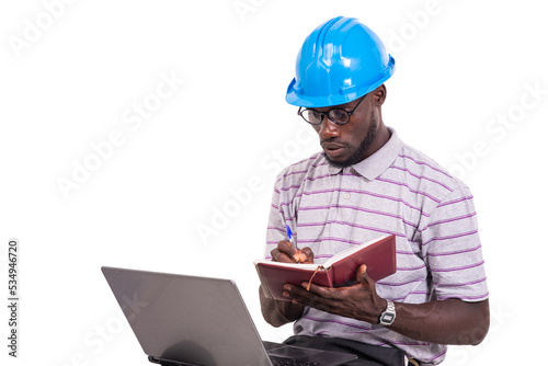 young man engineer writing in a notebook using a laptop.