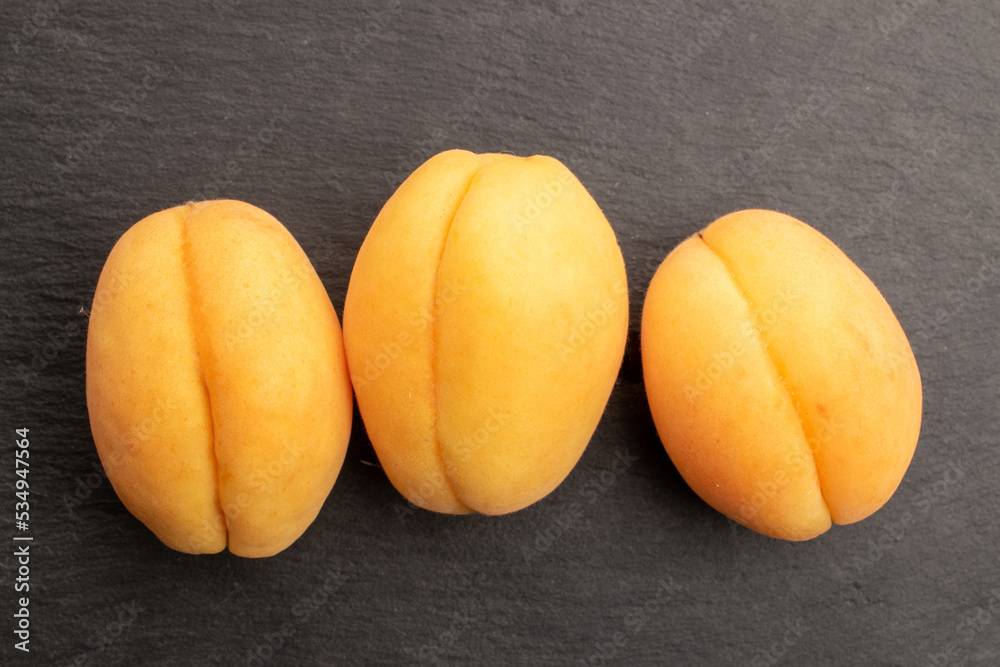 Three yellow pineapple apricots, close-up, on a slate board, top view.