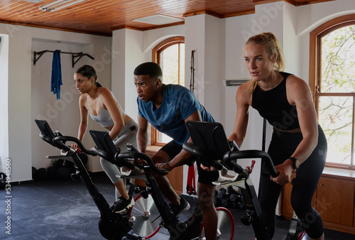 Three focused young multiracial adults doing cardio on exercise bike at the gym