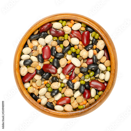 Mixed dried pulses in a wooden bowl  from above. Colorful mix of red kidney  black and white beans  mung beans  brown  green and red lentils  and chickpeas. Isolated  on white background  food photo.