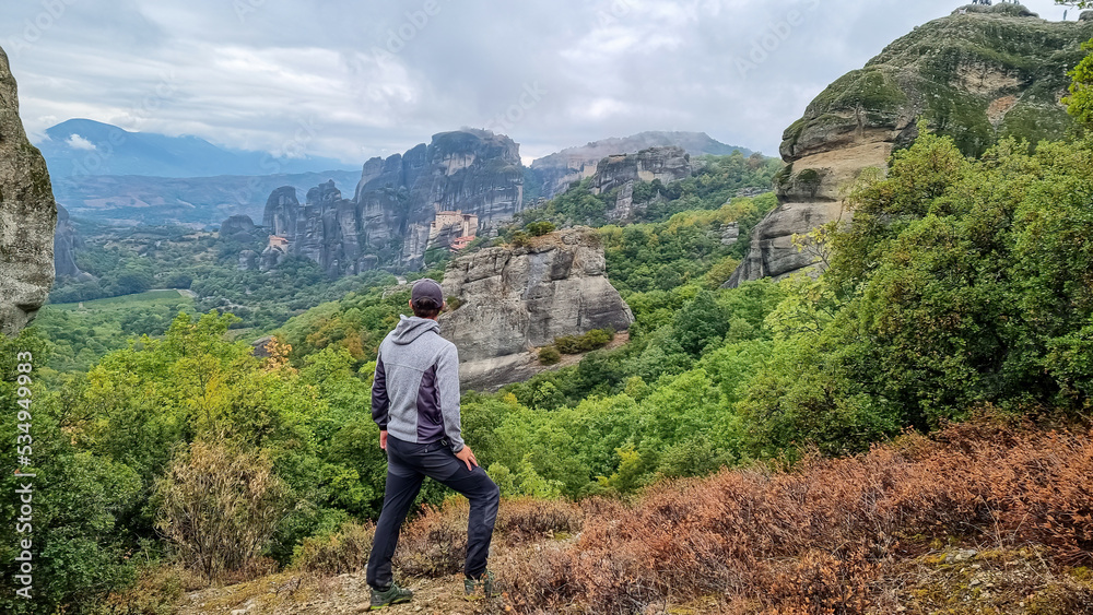 Man with scenic view of Holy Monastery St Nicholas Anapafsas and Monastery of Rousanos, Kalambaka, Meteora, Thessaly, Greece, Europe. Dramatic landscape atmosphere. Landmark build on rock formations