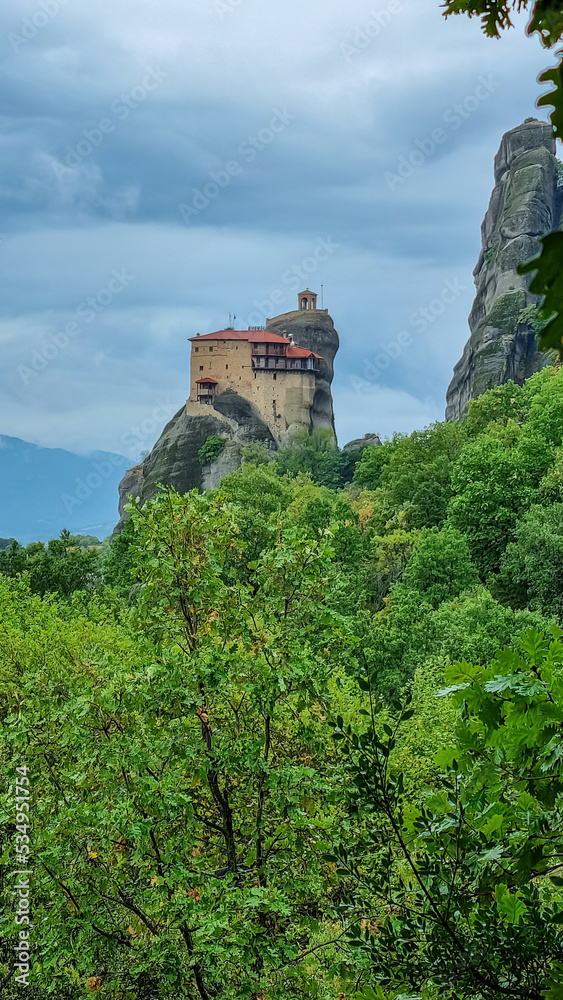 Scenic view of Holy Monastery of St Nicholas Anapafsas seen from forest near Kalambaka, Meteora, Thessaly, Greece, Europe. Dramatic landscape. Landmark build on rock formations. Tree branches in frame