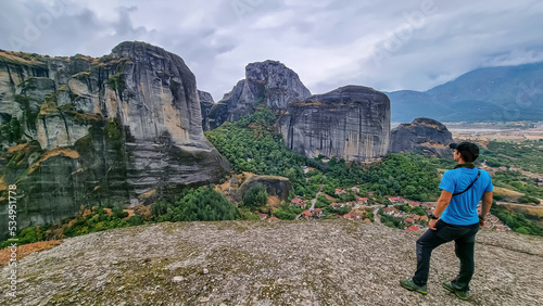 Man standing on top of rock summit Aghio Pnevma (Holy Spirit). Panoramic view on valley between village of Kastraki and Pindus mountains, Meteora, Kalambaka, Thessaly, Greece, Europe. Dramatic terrain photo