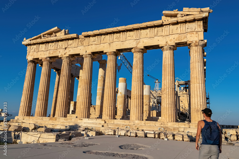 Rear view of tourist man looking at the Parthenon of the Acropolis of Athens, Attica, Greece, Europe. Ruins of ancient temple, the birthplace of democracy. No tourists on a sunny summer day, blue sky