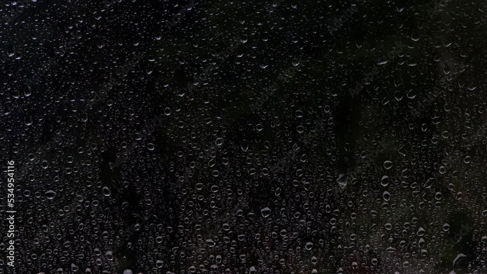 Textured dark background with rain drops falling on a window glass. High quality 4k footage