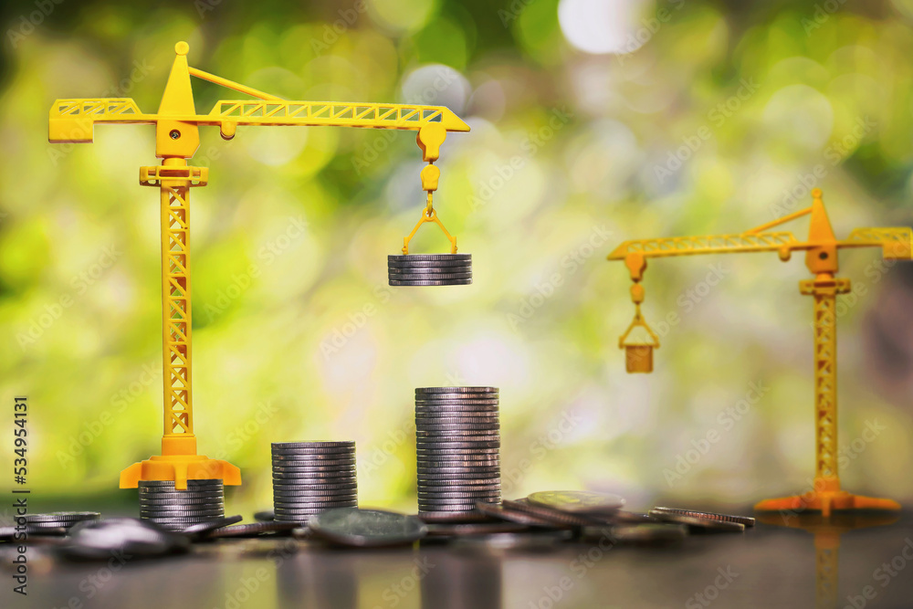 Construction cranes are stacking coins. business investment ideas - obrazy, fototapety, plakaty 