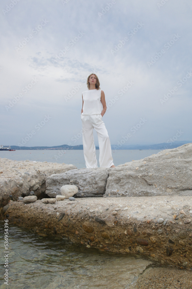 Fashion outdoor portrait of female model in white silk outfit on the beach