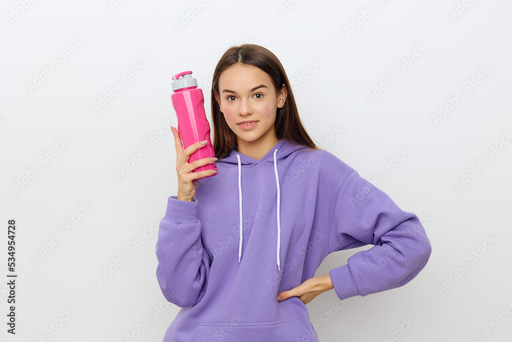 an interested woman stands on a white background in a purple suit holding a pink bottle in her hand, placing her other hand on her hip an interested woman stands on a white background in a purple suit holding a pink bottle in her hand, placing her other hand on her hip