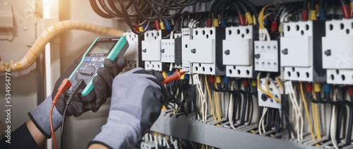 Electricity and electrical maintenance service, Engineer hand holding AC multimeter checking electric current voltage at circuit breaker terminal and cable wiring main power distribution board. photo