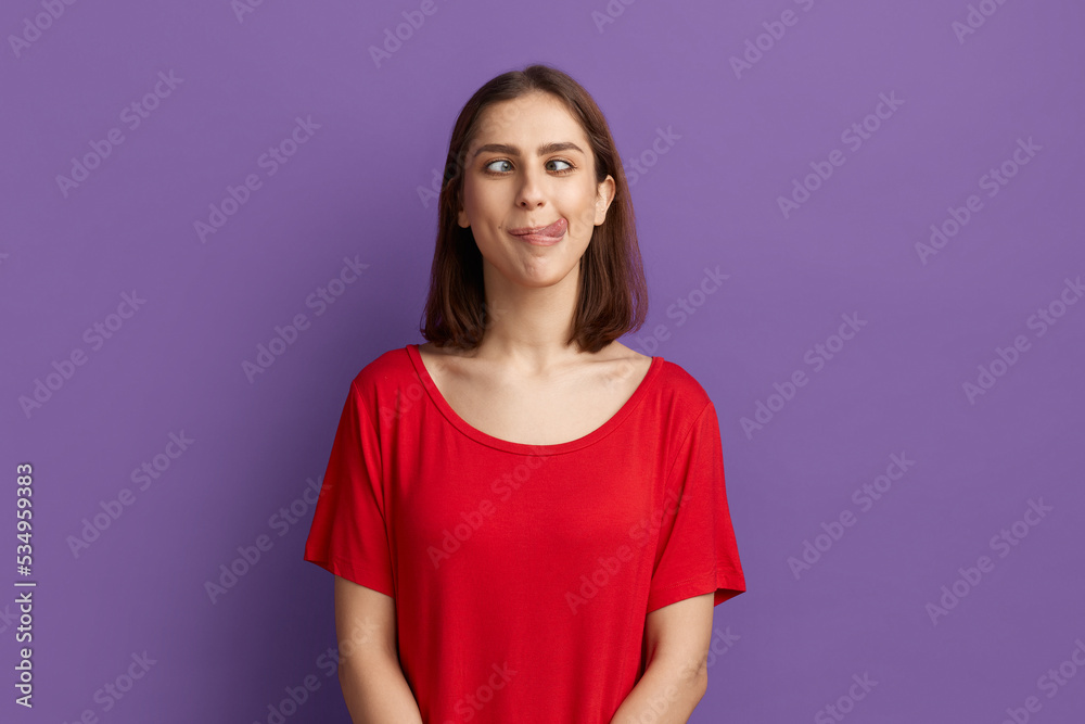 I lost my mind. Pretty brunette girl in red t-shirt demonstrating tongue and making stupid face with crossed eyes. Looks as a crazy woman showing ridiculous grimace. Posing over purple background. I lost my mind. Pretty brunette girl in red t-shirt demonstrating tongue and making stupid face with crossed eyes. Looks as a crazy woman showing ridiculous grimace. Posing over purple background.