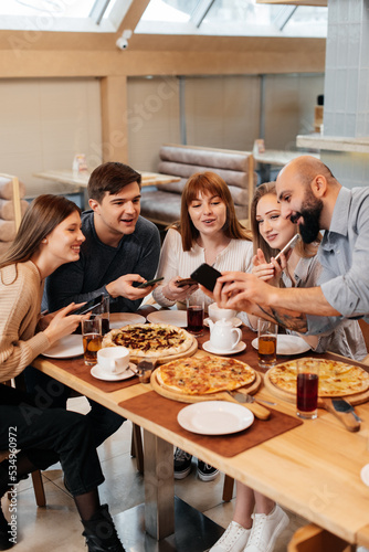 A group of friends is having pizza in a cozy restaurant and taking selfies, taking pictures together. A cheerful group of friends.