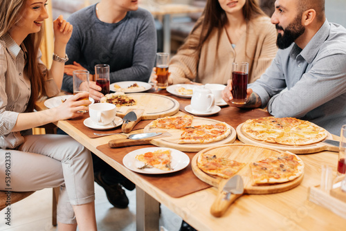 A cheerful group of friends is eating delicious pizza in a restaurant. Friends are sitting in a restaurant and having fun.