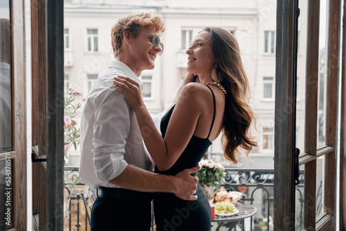 Happy young couple in formalwear embracing while standing on the balcony together