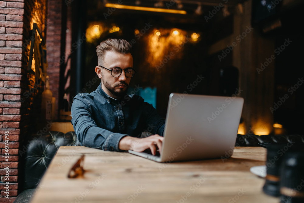 young male IT specialist with a beard and hairstyle works with a laptop in a cozy cafe. Online work on the Internet. young male IT specialist with a beard and hairstyle works with a laptop in a cozy cafe. Online work on the Internet.