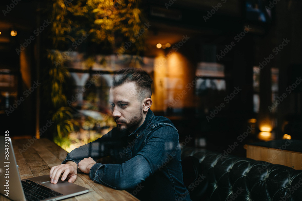young male IT specialist with a beard and hairstyle works with a laptop in a cozy cafe. Online work on the Internet. young male IT specialist with a beard and hairstyle works with a laptop in a cozy cafe. Online work on the Internet.