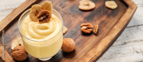 Glass of tasty pudding with banana and nuts on wooden background, closeup