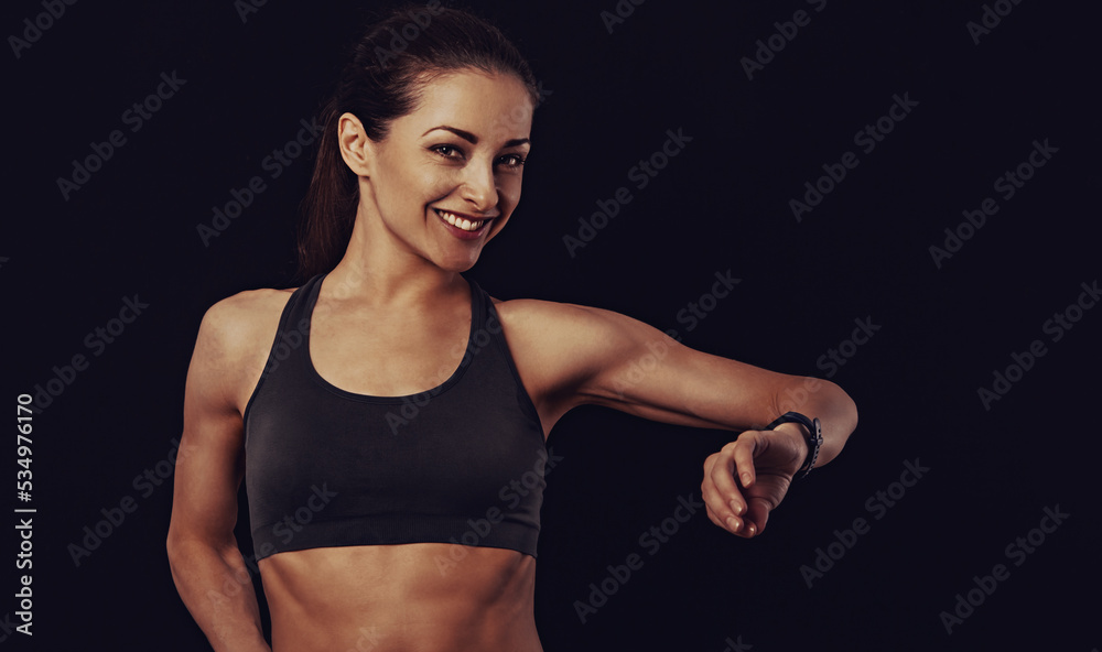 Happy smiling fit healthy fitness woman in bra top clothing looking on sporty watches what time is it now on black background with empty copy space. Closeup Happy smiling fit healthy fitness woman in bra top clothing looking on sporty watches what time is it now on black background with empty copy space. Closeup