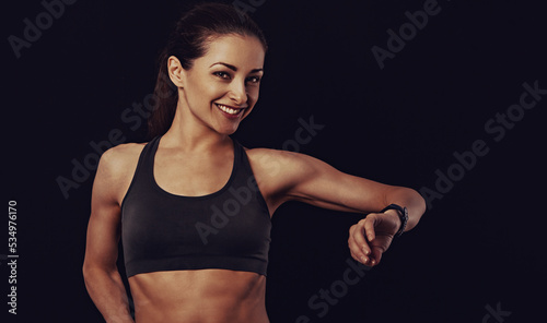 Happy smiling fit healthy fitness woman in bra top clothing looking on sporty watches what time is it now on black background with empty copy space. Closeup © nastia1983