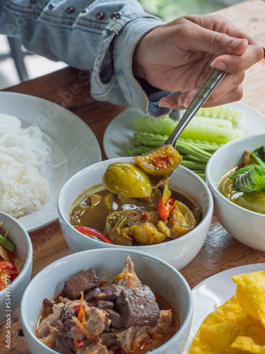 Thai eggplant red curry, a woman scoops Thai food with a spoon, selective focust. Thai food concept.