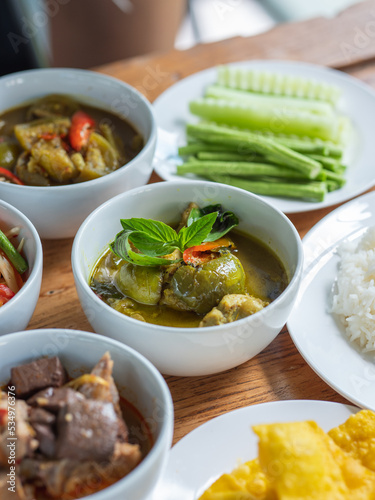 Green curry in a white ceramic cups is served alongside other Thai dishes on the table. Thai food, selective focus.