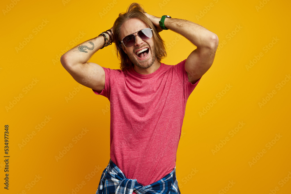 Handsome young man pointing away and smiling while standing against yellow background Handsome young man pointing away and smiling while standing against yellow background