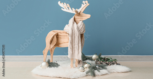 Wooden reindeer with scarf and Christmas decorations near blue wall in room