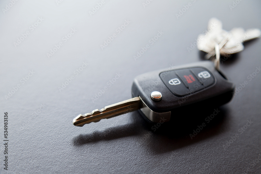 Car key on top of a black table with natural light. Key with buttons to lock and unlock the door. Car key concept. Door lock concept. Copy space. Car key on top of a black table with natural light. Key with buttons to lock and unlock the door. Car key concept. Door lock concept. Copy space.