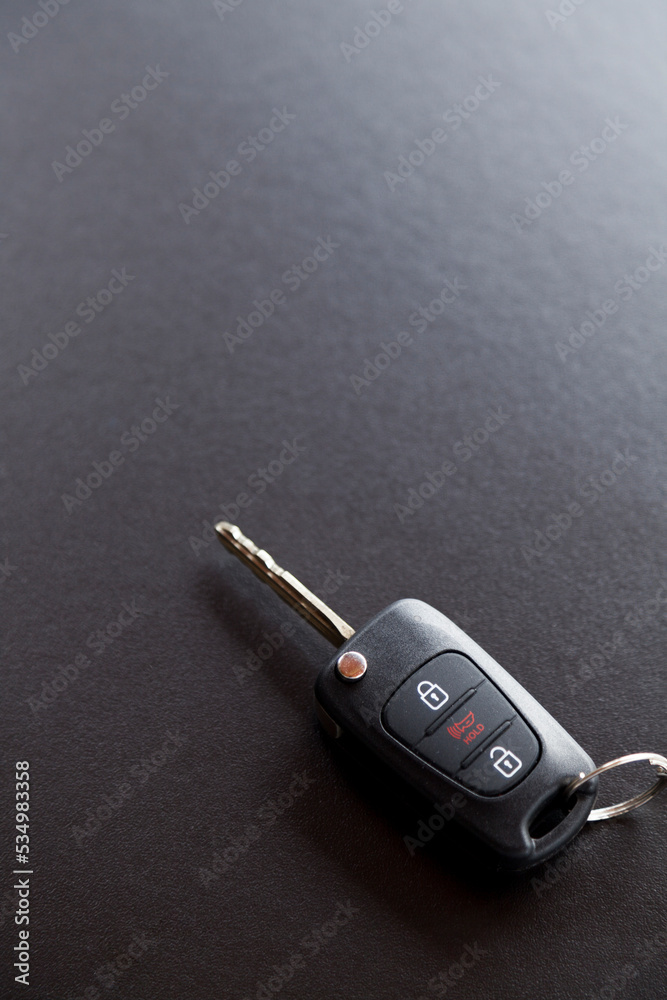 Car key on top of a black table with natural light. Key with buttons to lock and unlock the door. Car key concept. Door lock concept. Copy space. Car key on top of a black table with natural light. Key with buttons to lock and unlock the door. Car key concept. Door lock concept. Copy space.
