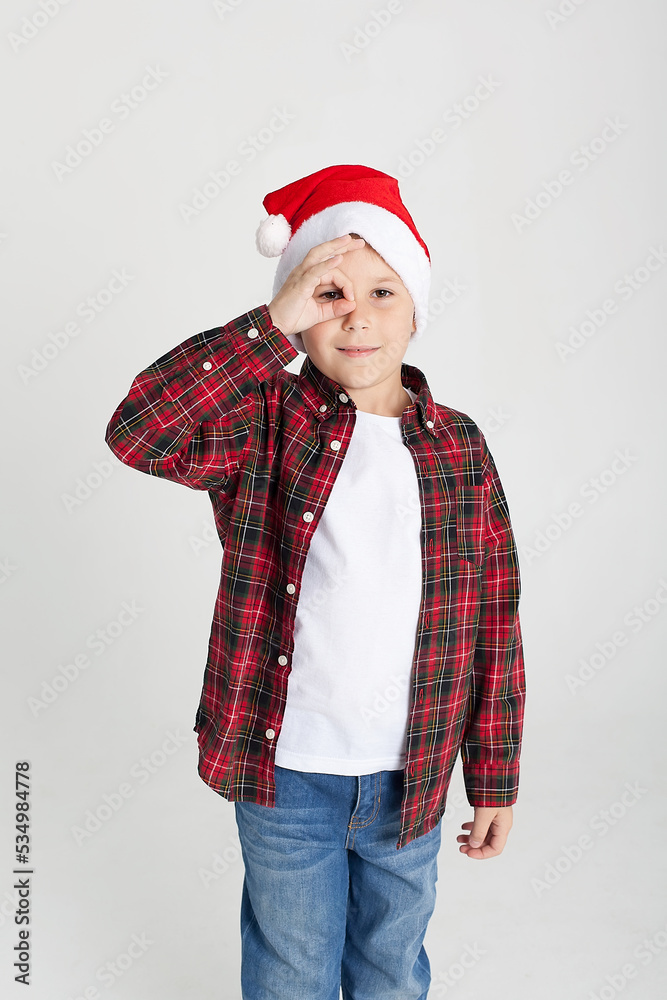 The charming seven year old boy in red Santa Claus cap smiles, having stretched hands up. The photo is executed by isolated. The charming seven year old boy in red Santa Claus cap smiles, having stretched hands up. The photo is executed by isolated.