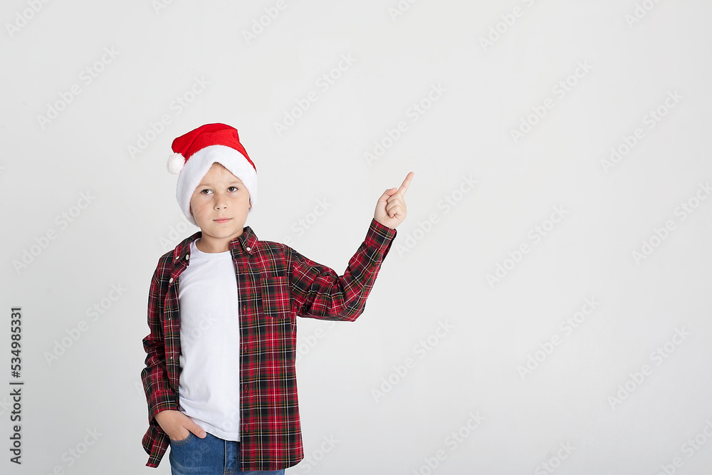 The charming seven year old boy in red Santa Claus cap smiles, having stretched hands up. The photo is executed by isolated.